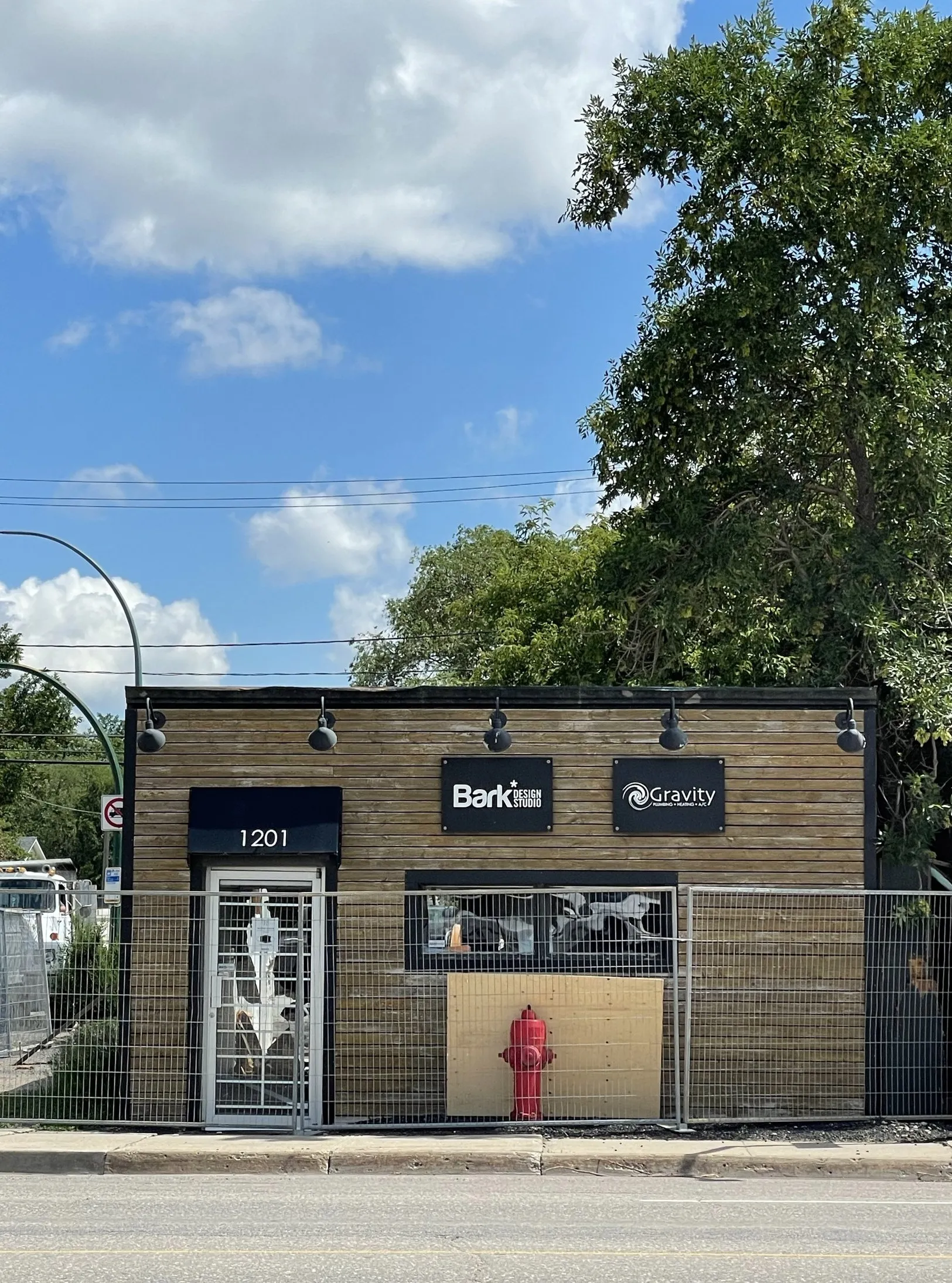 The old single-storey building at 1201 Winnipeg Street in 2021, fenced off, with the Bark and Gravity signs and the red fire hydrant out front