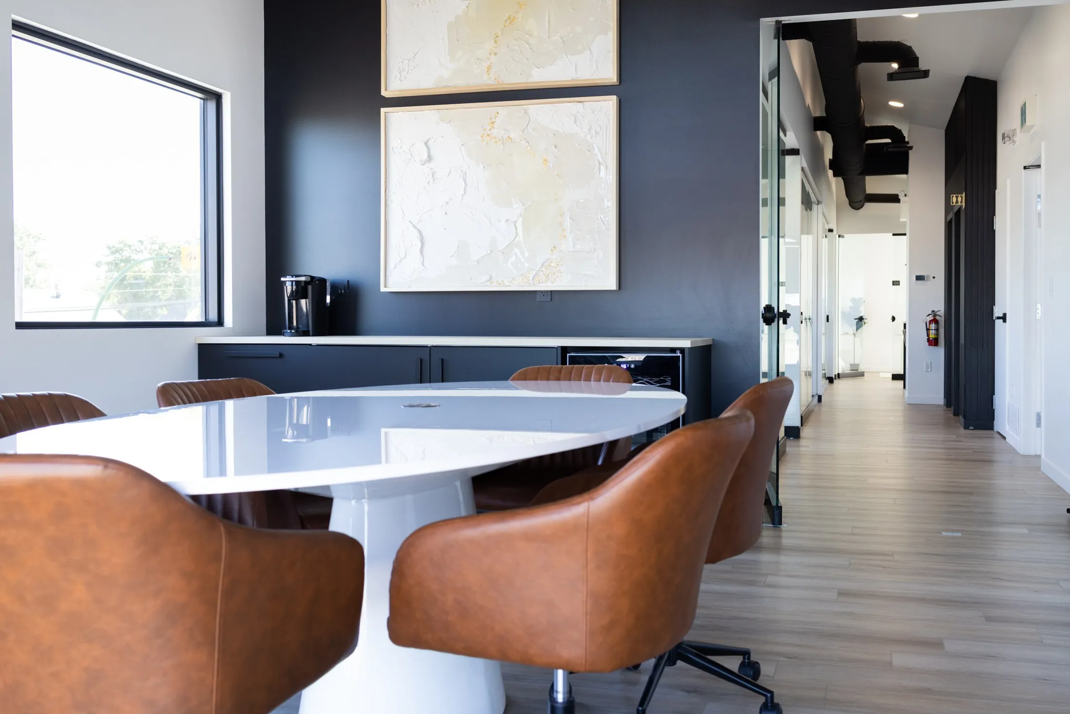 The white oval table and leather chairs, the side counter with the coffee maker behind