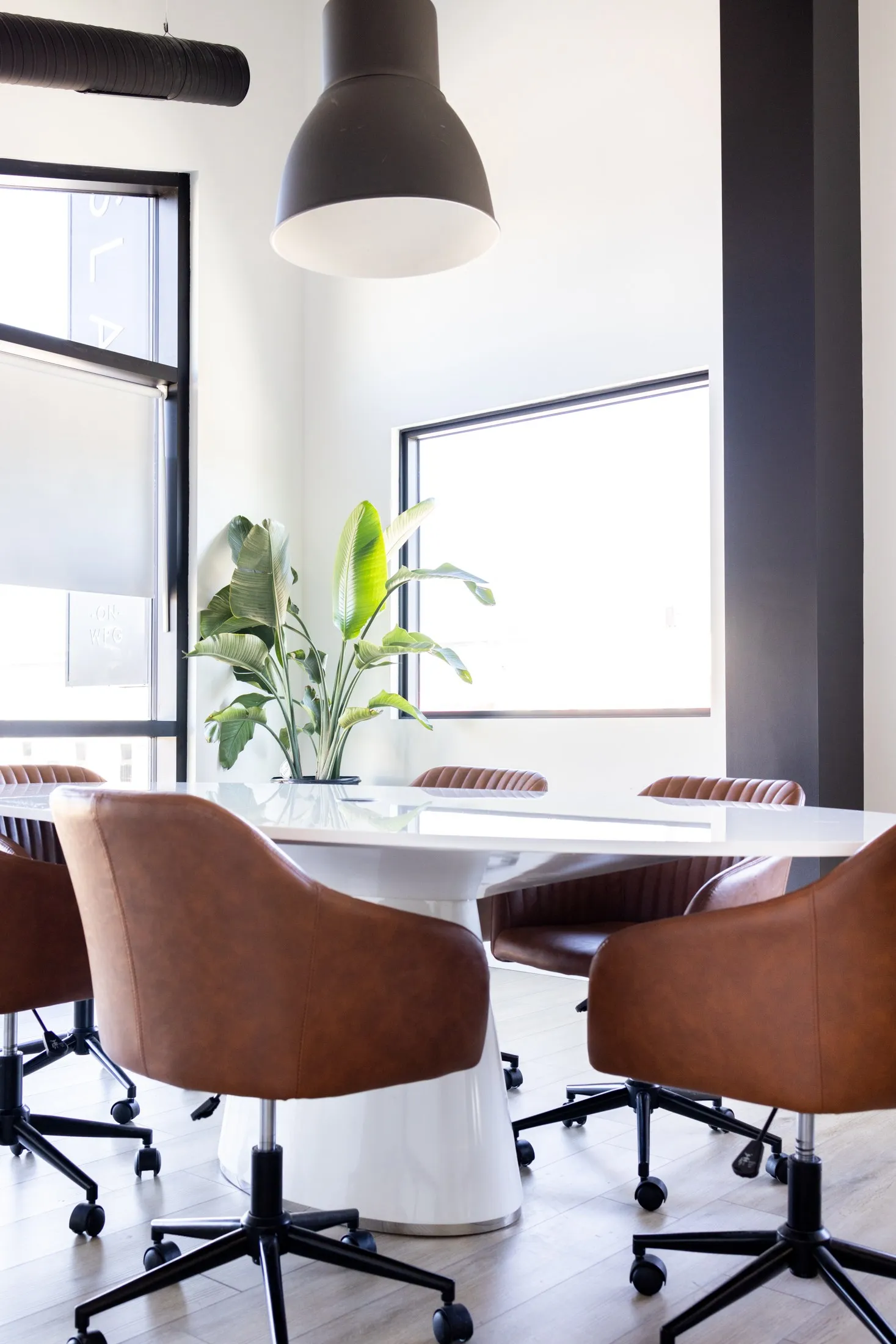The boardroom table and tan leather chairs under a pendant light, windows on two walls