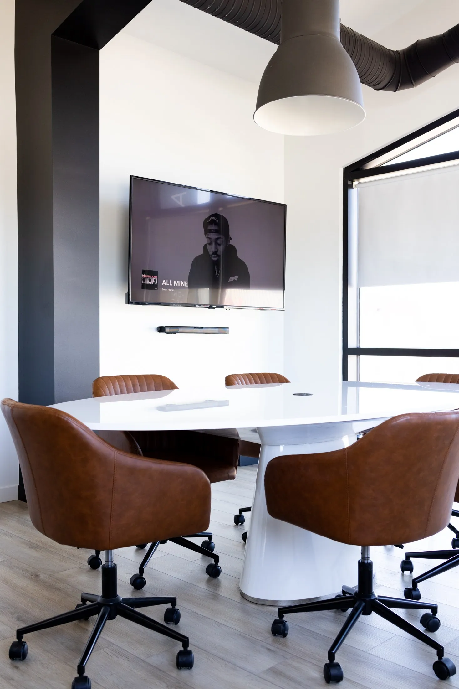 The screen on the dark wall at the end of the boardroom, the table and chairs below the tall windows