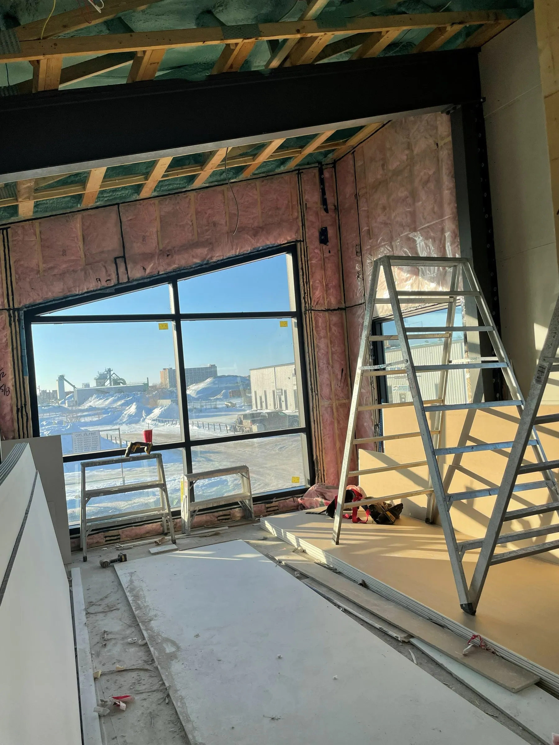 The boardroom under construction: insulation in the walls, a bare floor, ladders, and the tall slanted window looking out on a snowy street