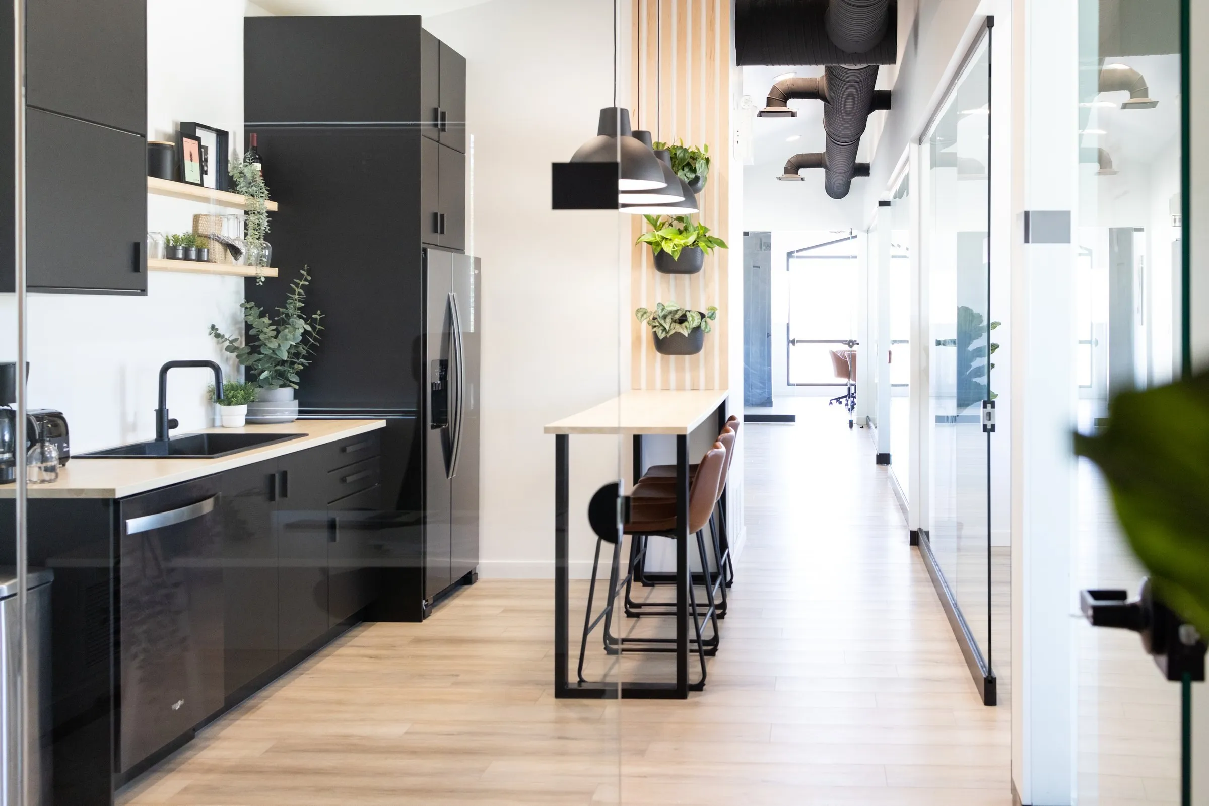 The shared kitchen, black cabinets and a wood bar under pendant lights, the office hallway beyond